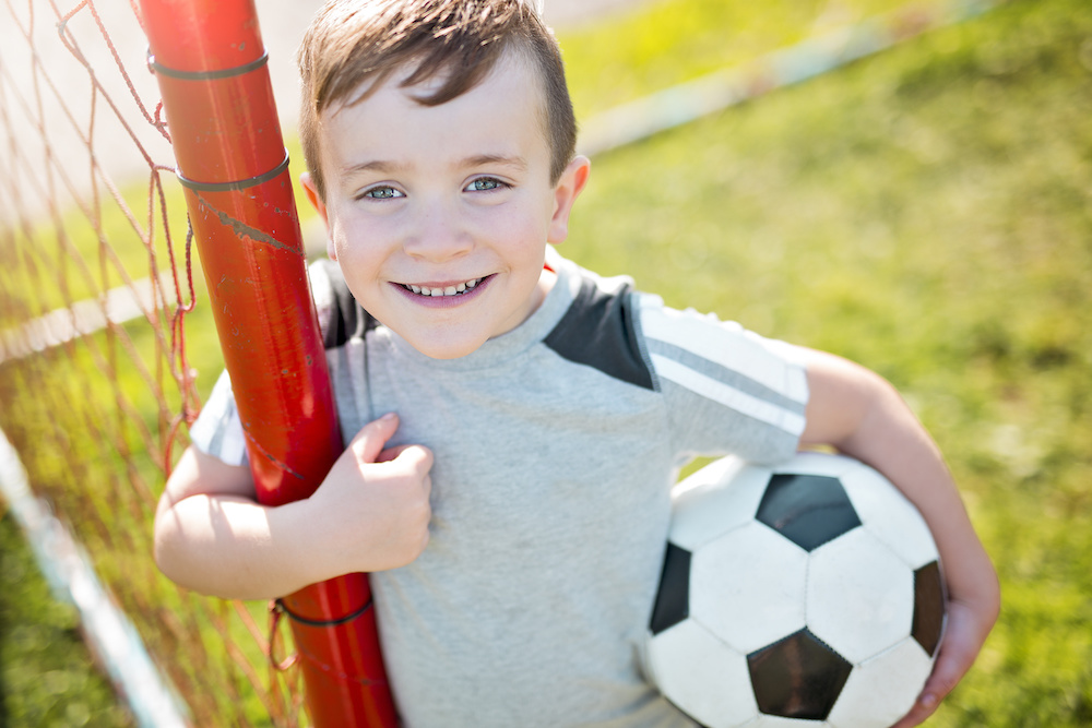 young boy holding soccer ball - needs school sports physicals