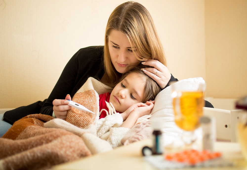 Young mother checking temperature of daughter in bed, sick with cold and flu symptoms