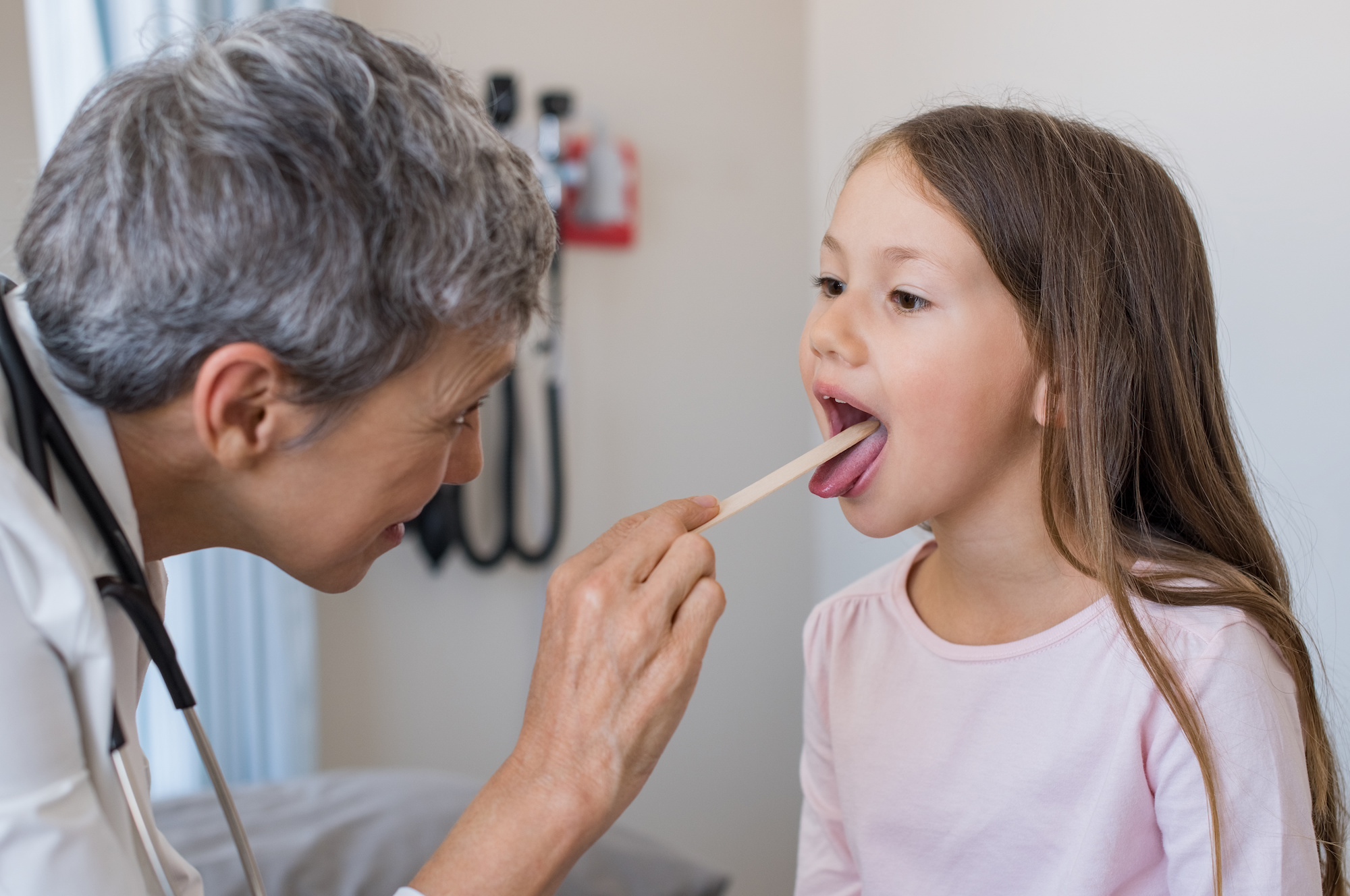 Woman doctor examining little girl mouth for strep throat